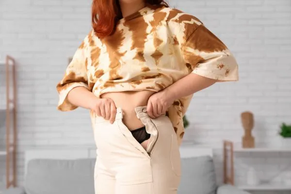 Image of woman trying to do her trousers up after pregnancy weight gain Ware