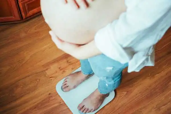 Image of woman weighing herself and experiencing weight gain through pregnancy Ware